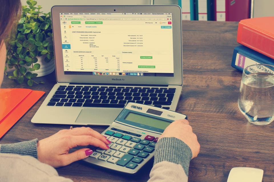 Manos con una calculadora junto a un portátil
